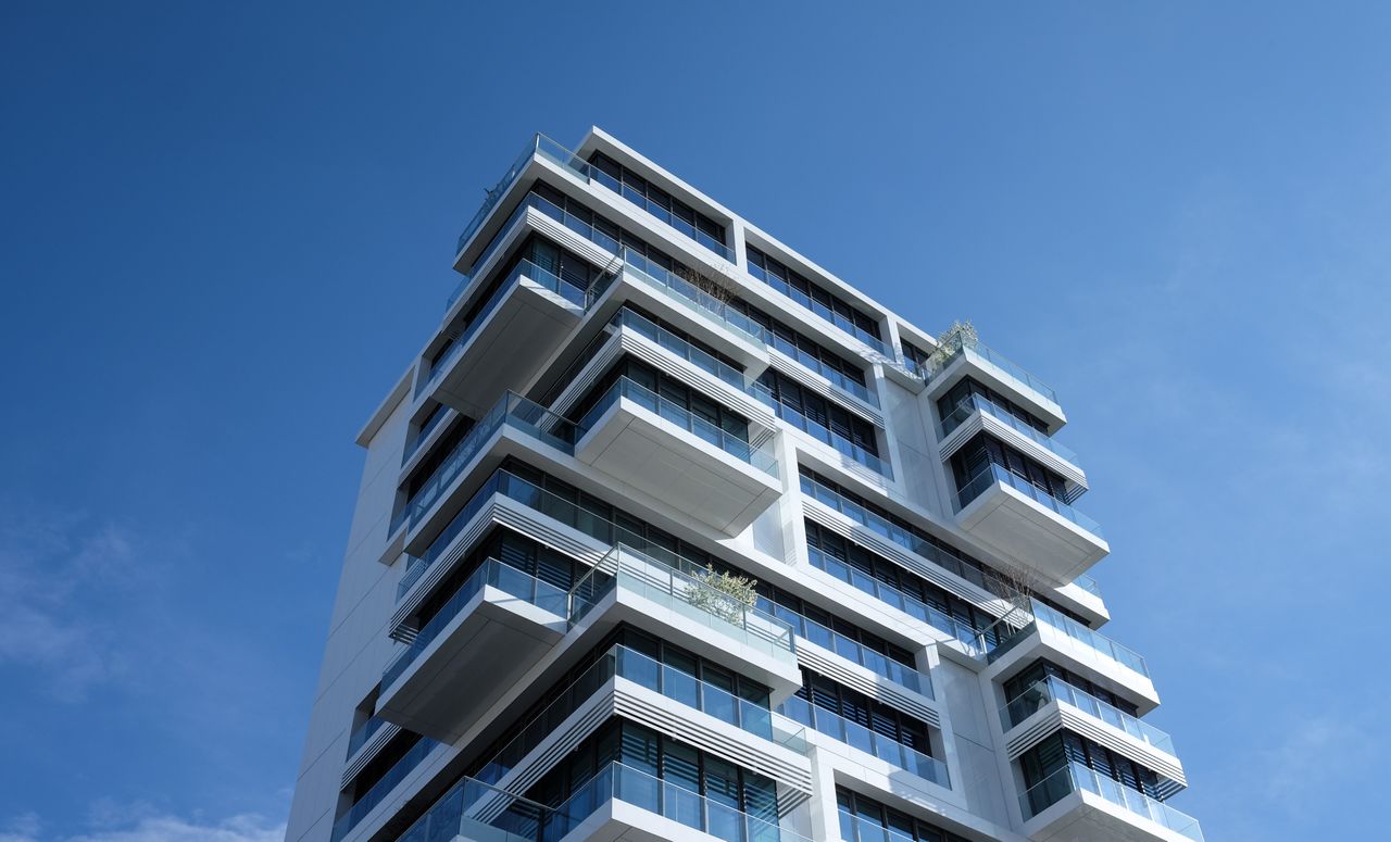 Home Striking low-angle shot of a modern condominium with unique balcony design and clear blue sky.